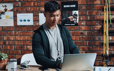 Personal Trainer plant am Laptop Trainingseinheiten, an der Ziegelwand hängen Trainingspläne