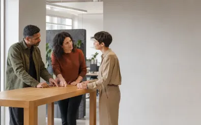 Drei Berufstätige im Gespräch an einem Stehtisch im Büro