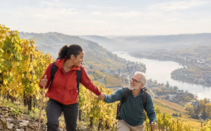 Eine Frau reicht auf den Stufen eines Moselweinbergs einem älteren Mann die Hand zurück und nimmt ihn mit nach oben