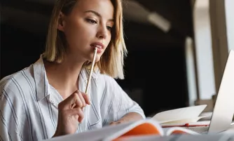 International Management Studium Eine Frau sitzt nachdenklich vor ihrem Laptop und hält ihren Stift vor ihrem Mund