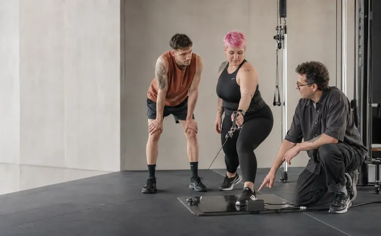 Trainerin korrigiert im Studio die Übungstechnik an einer Kraftstation