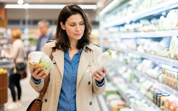 Frau vergleicht im Supermarkt die Angaben auf zwei Lebensmittelverpackungen