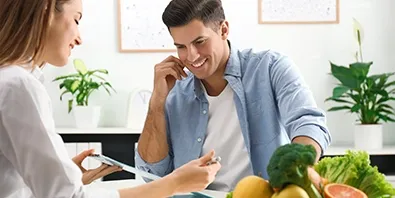 Beraterin und Klient im Gespräch, auf dem Tisch Obst, Gemüse und ein Maßband
