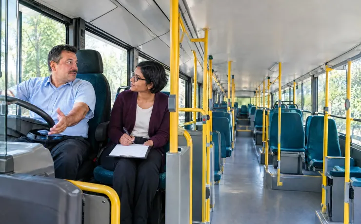 Arbeitspsychologin hört im leeren Linienbus einem Busfahrer zu, der ihr seinen Arbeitsalltag beschreibt