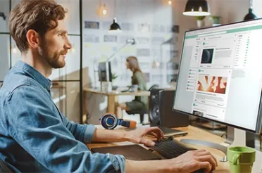 Mann am Schreibtisch prüft am Bildschirm die Beiträge eines Social-Media-Kanals