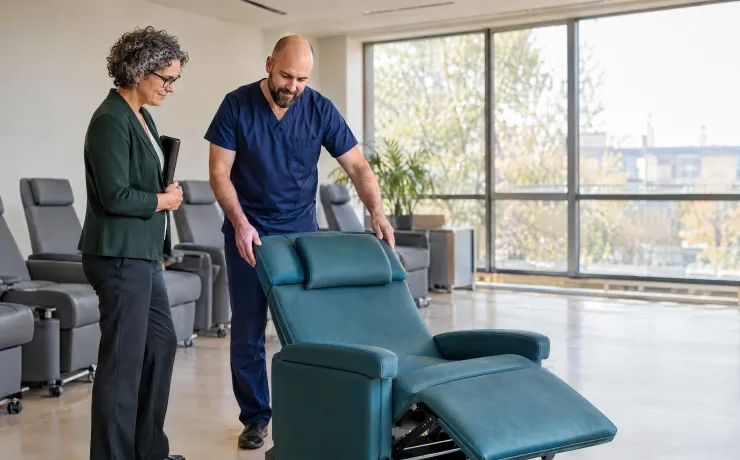 Pflegeleiter führt im Ruhebereich eines ambulanten OP-Zentrums einen neuen Liegesessel vor, die Gesundheitsökonomin nickt