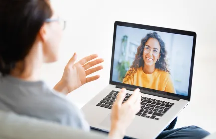 Eine Studierende spricht zu Hause per Videoanruf mit einer lächelnden Frau, die auf dem Laptopbildschirm zu sehen ist.