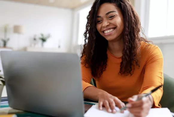 Ohne Numerus Clausus an der EHiP studieren Eine Frau sitzt am Schreibtisch und schaut lachend in ihren Laptop