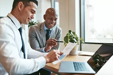 Zwei Businessmänner sitzen vor einem Laptop und besprechen eine Statistik