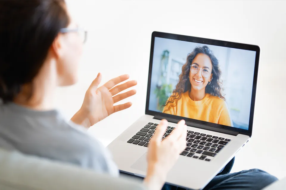 Eine Studierende spricht zu Hause per Videoanruf mit einer lächelnden Frau, die auf dem Laptopbildschirm zu sehen ist.
