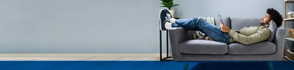 Ein Mann liegt entspannt auf einem grauen Sofa, die Füße hochgelegt, und liest auf einem Tablet.