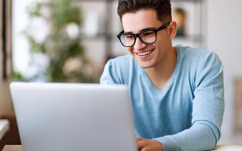 Ein junger Mann mit Brille lächelt beim Arbeiten an seinem Laptop.