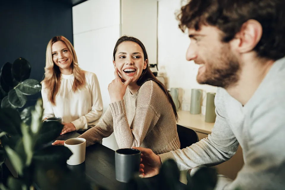Drei lachende Kolleginnen und Kollegen sitzen bei Kaffee und Tee an einem Tisch und unterhalten sich.