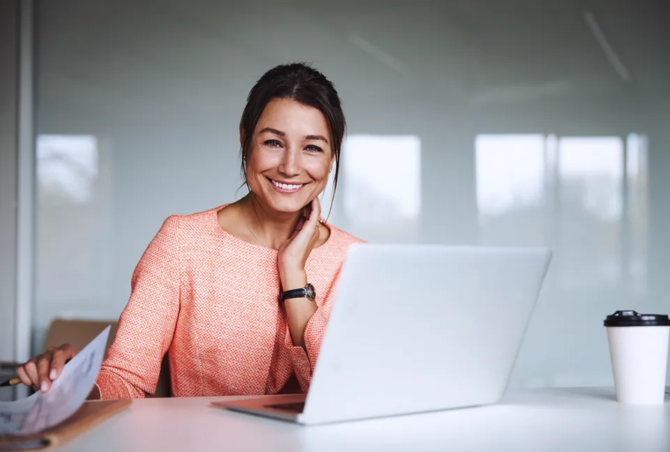 Frau im Businesslook arbeitet am Laptop und lächelt