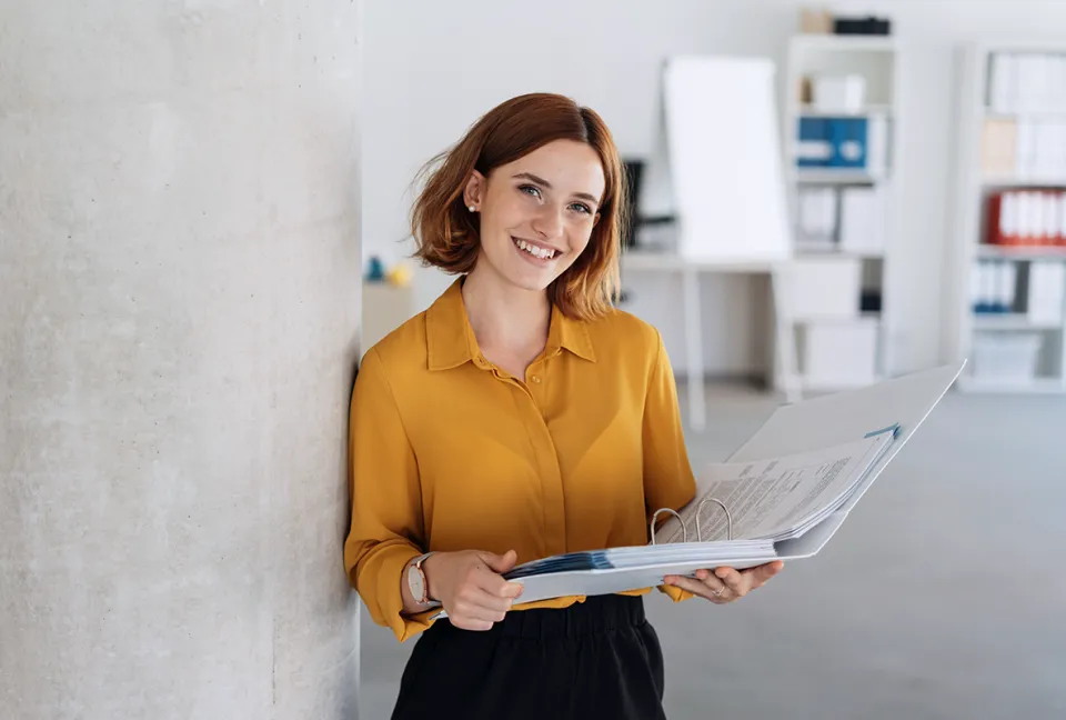 Eine Businessfrau hält einen Ordner in der Hand und lacht in die Kamera