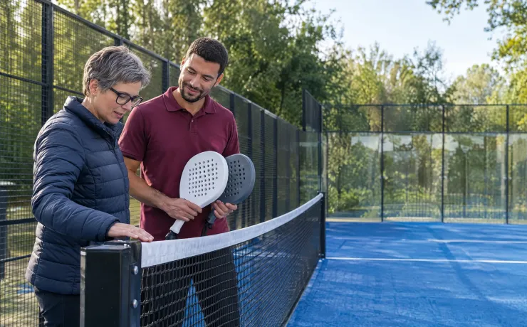 Sportmanagerin prüft bei der Abnahme der neuen Padel-Plätze die Netzkante, daneben der künftige Abteilungsleiter mit zwei Schlägern