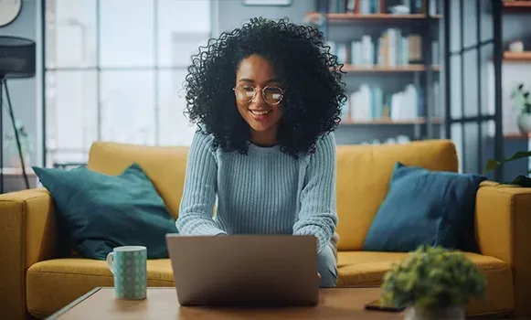 Frau sitzt im Wohnzimmer vor ihrem Laptop und bereitet sich für ihr Digitalisierungs Studium vor.