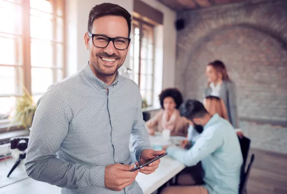 Projektmanager*in Mann im Businesslook hält Handy in der Hand und lächelt in die Kamera