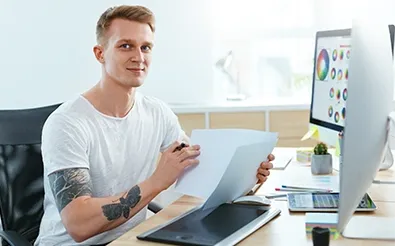 Mann arbeitet am Schreibtisch mit Grafiktablett und einem Monitor voller Farbpaletten an einem Digital-Design