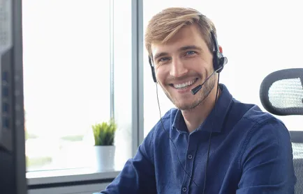 Ein Mitarbeiter der Studienberatung mit Headset sitzt am Arbeitsplatz und schaut lächelnd in die Kamera.