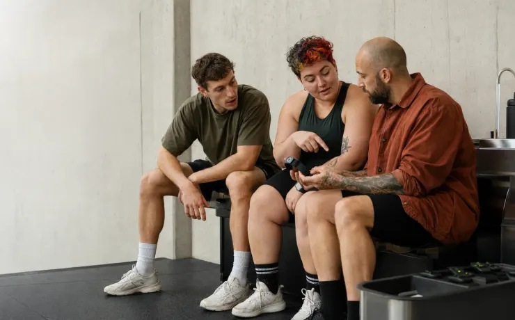 Drei Personen besprechen im Trainingsbereich die Daten eines Aktivitätstrackers