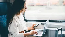 Eine Gruppe sitzt lachend und im Austausch an einem Holztisch mit Laptops, Notizen und Kaffeebechern.