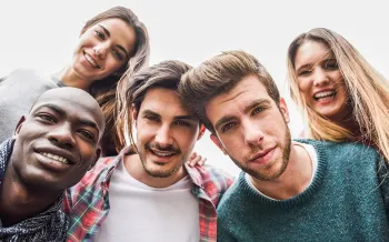 Fünf junge Menschen lächeln dicht beieinander in die Kamera, aufgenommen von unten.