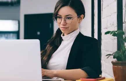 Eine Frau und ein Mann sitzen lächelnd an einem Tisch mit Notizbuch und Laptop und arbeiten gemeinsam.
