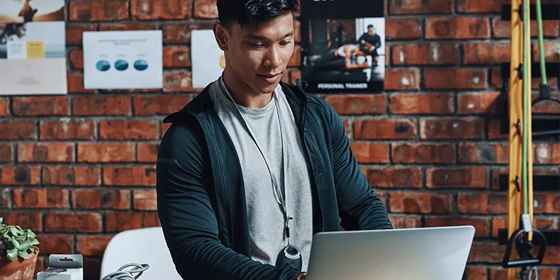 Personal Trainer plant am Laptop Trainingseinheiten, an der Ziegelwand hängen Trainingspläne