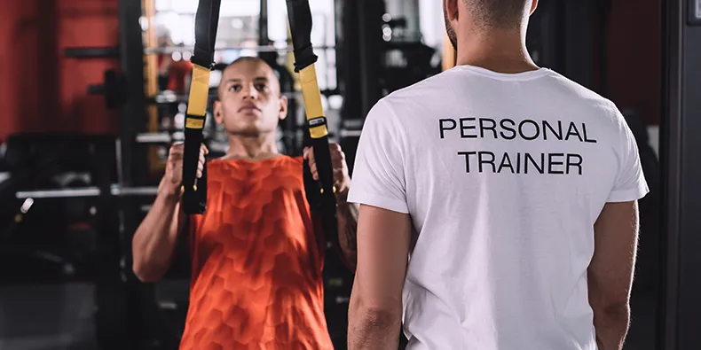 Personal Trainer betreut einen Kunden beim Schlingentraining im Fitnessstudio