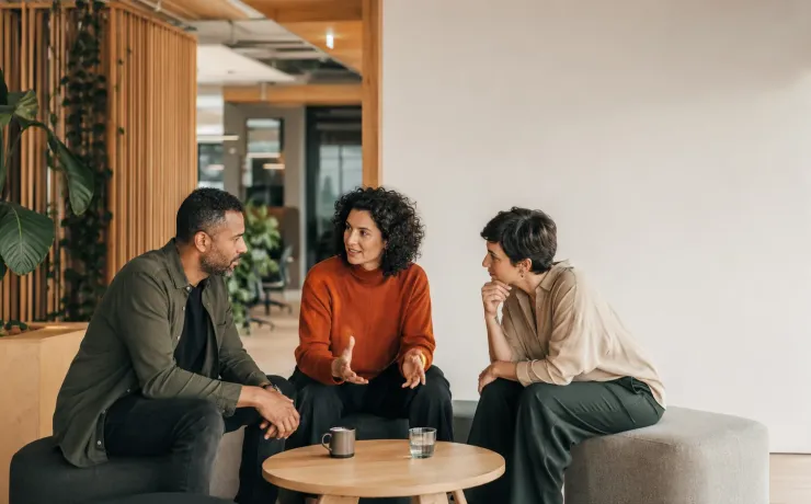 Drei Berufstätige sitzen in einer offenen Bürolounge und besprechen sich
