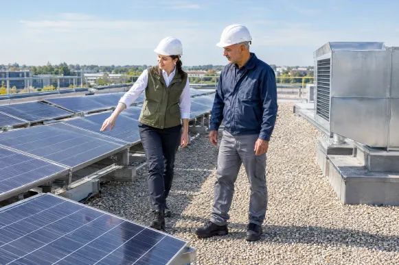 Nachhaltigkeitsmanagerin prüft mit dem Facility-Manager auf dem Dach eines Betriebs die Verschattung einer Solarmodulreihe