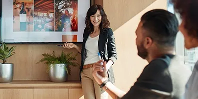 Eine Businessfrau steht vor einem Bildschirm und spricht vor mehreren Personen