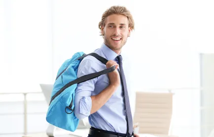 Ein Mann im Hemd mit Krawatte trägt eine hellblaue Tasche über der Schulter und blickt lächelnd zur Seite.