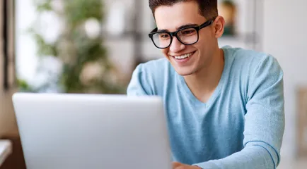 Ein junger Mann mit Brille lächelt beim Arbeiten an seinem Laptop.
