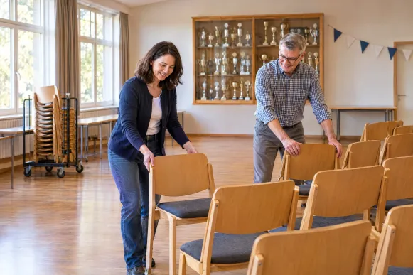 Geschäftsführerin und Vorsitzender stellen im Vereinsheim die Stühle für die Mitgliederversammlung in Reihen